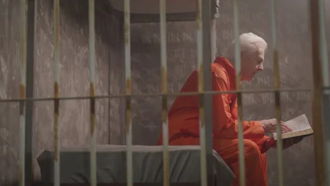Elderly Criminal Sits in a Jail Cell and Opens up the Bible Stock Footage 208744063