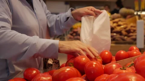 An elderly customer chooses tomatoes, adding them into a plastic bag. The hands Stock Footage 313485606