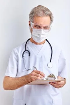 Elderly doctor man makes notes wearing stethoscope isolated on white Stock Photos