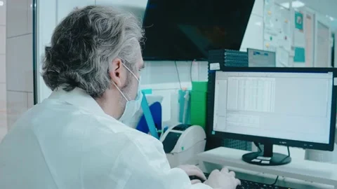 Elderly doctor works on a computer with documents in a white laboratory Vídeo Stock 166664357