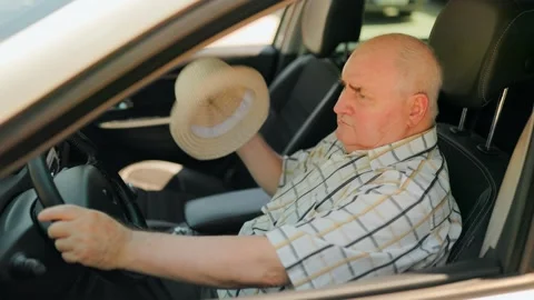 Elderly driver feeling hot and fanning himself with a hat inside the car. Stock Footage 343264213