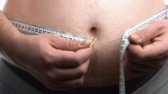 Obese man measuring waist with tape measure - SuperStock