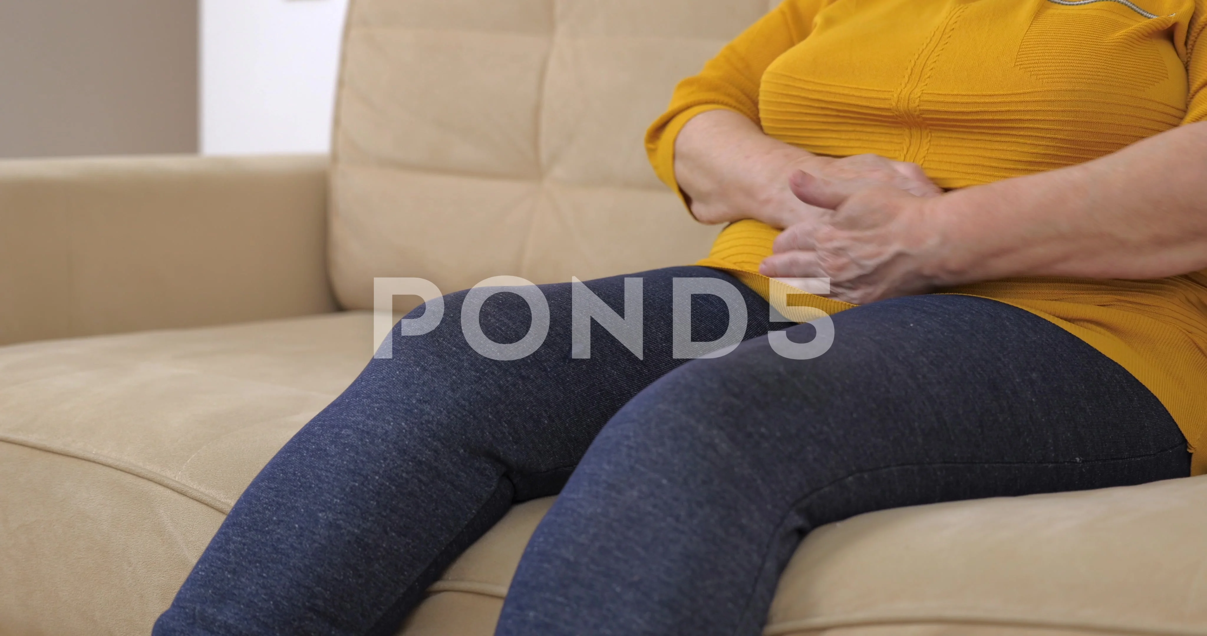 Elderly fat woman having painful stomach ache sitting on sofa.