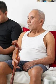 Elderly father holding cane while sitting with son showing mobility limitat.. 写真素材