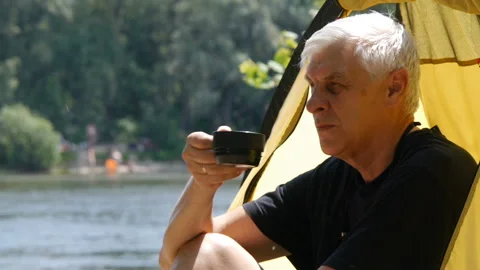 Elderly gray haired camper man sitting in the tent, drinking tea. Close up Video stock 112377210