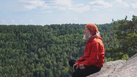 An elderly gray-haired man with a beard, a hipster traveler sits on a rock, r Foto stock