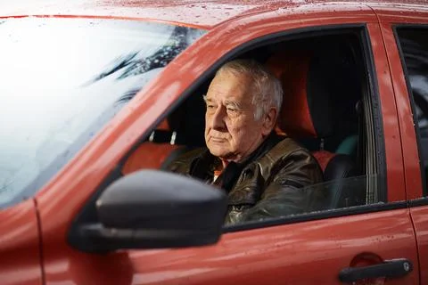 Elderly gray-haired man is driving his orange car in late autumn Stock Photos