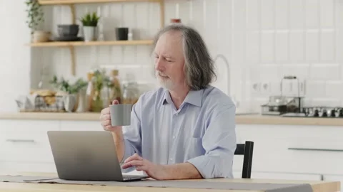 Elderly gray-haired man enjoys delicious coffee while sitting at home near a Stock Footage 237696376