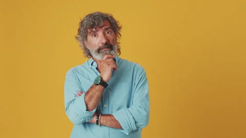Elderly gray-haired man listens attentively and agrees, isolated on orange Stock Footage 250841192