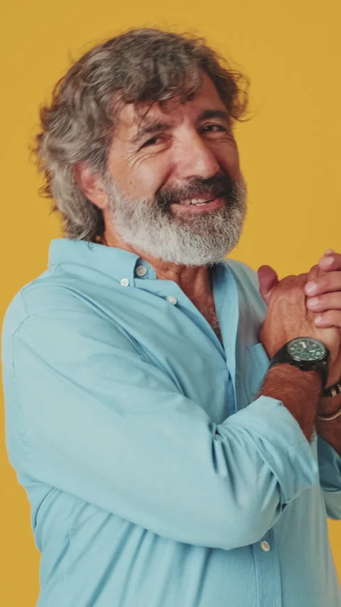 Elderly gray-haired man put hands on chest, it's so cute, isolated on orange Stock Footage 250841237