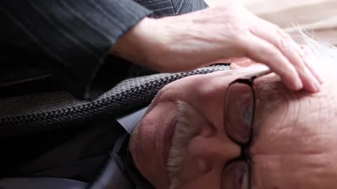 An elderly gray-haired man sitting on a chair in a room by the window, his head Video stock 252418275