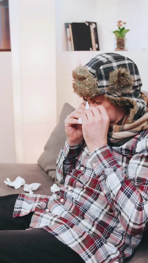 An elderly gray-haired man in a warm earflap hat sneezes and coughs into a Stock Footage 301582016