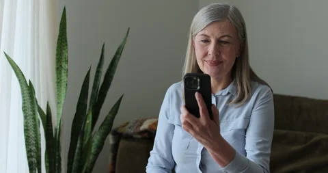 Elderly gray-haired woman using smartphone for video call. 库存影片 334059863