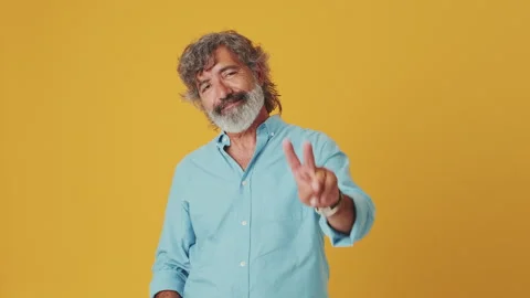 Elderly grey-haired man looking at camera smiling showing victory sign isolated Stock Footage 248272897