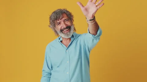 Elderly grey-haired man looking at the camera and waving his palm, isolated on Stock Footage 252503454