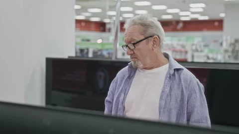 An elderly grey-haired man of retirement age is choosing a TV set in a consumer Stock Footage 252120228