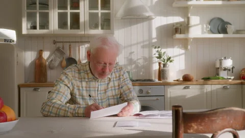 Elderly grey haired man sits at table with papers Video stock 264836710
