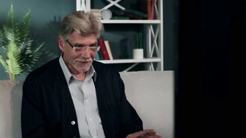 An elderly grey-haired man is watching TV and cheering excitedly. An old man in Video stock 132668143
