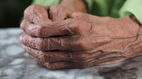 Elderly hands resting on a marble table in a simple setting Stock Footage 346665938