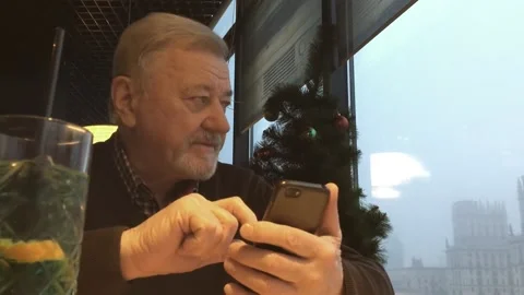 Elderly handsome senior with a gray beard near the Christmas tree, scroll phone, Stockbeeldmateriaal 222577997