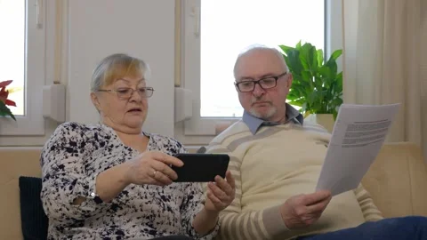 An elderly immigrant couple sits on a sofa holding documents in their hands Stock Footage 303728237
