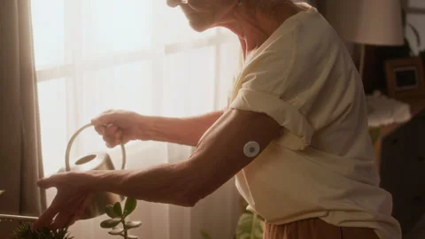Elderly Lady with Diabetic Sensor Patch Watering Potted Plants at Home Vídeos de archivo 320968975
