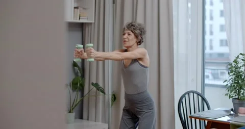 Elderly lady is doing energizing dumbbell exercises at home, fitness training Video stock 231798651