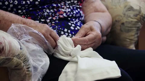 An elderly lady's hand cutting extra threads from a piece of white fabric Stock Footage 156721672