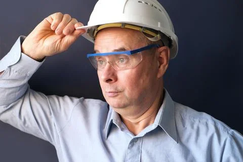 Elderly male engineer, builder in protective helmet, glasses looking seriousl Stock Photos