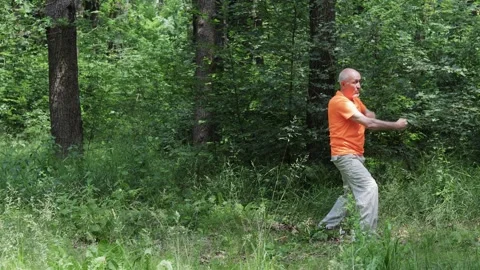 An elderly man actively performs formal exercises against a natural backdrop Stock Footage 311150894