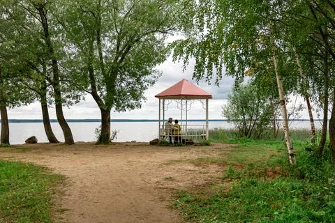 An elderly man and a woman in love relax in a gazebo on the lake shore Stock Photos