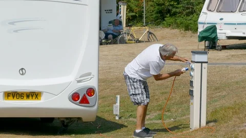 Elderly man attaching a power cable on a campsite. Video stock 93079583