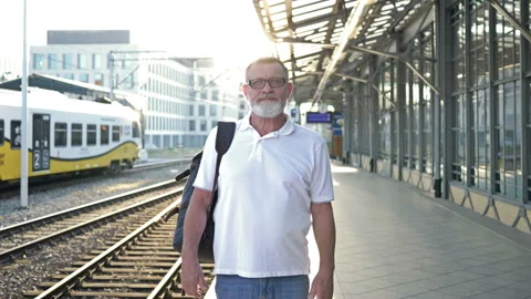An elderly man with a backpack stands on the platform waiting for his train. Stock Footage 138351605