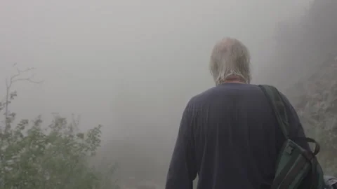Elderly man with backpack walking on a misty mountain trail Stock Footage 331659120
