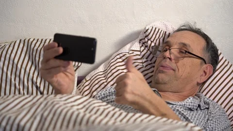 Elderly Man in Bed with Smartphone. Remote Communication with Family and Friends Stock Footage 144683317