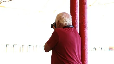 An elderly man with a camera stands with his back Stock Footage 84550614