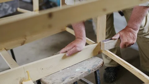 Elderly man carpenter builds a small boat with his hands out of wood in a small Stock-Footage 89785798