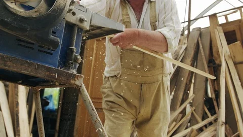 Elderly man carpenter builds a small boat with his hands out of wood in a small Vídeos de archivo 89785992