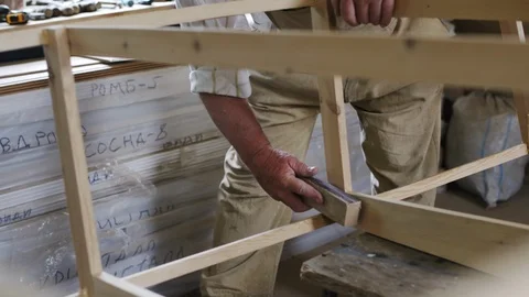 Elderly man carpenter builds a small boat with his hands out of wood in a small Видео 89786561