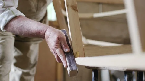 Elderly man carpenter builds a small boat with his hands out of wood in a small Vídeo Stock 89786726