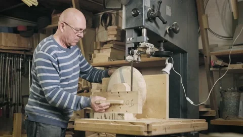 An elderly man in a carpentry workshop saws off the remains of a wooden Stock Footage 203807435