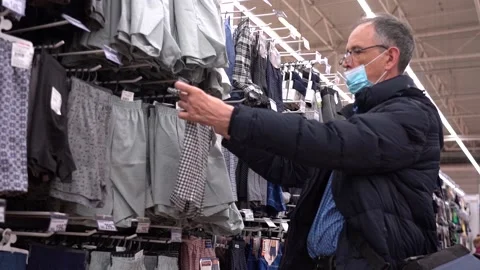 An elderly man chooses clothes in a store. An elderly man wearing a mask due to Stock Footage 168430743