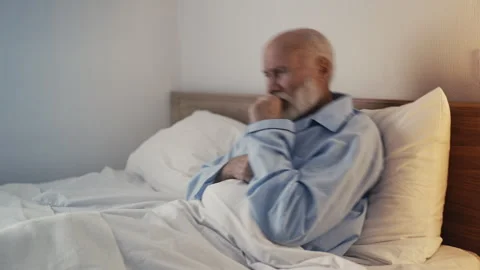 Elderly man coughing while sitting in bed, suffering from bronchitis and illness Stock Footage 310009136
