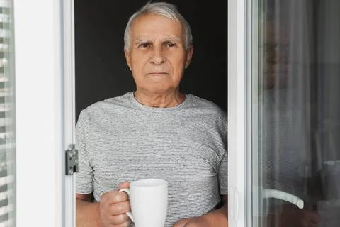 Elderly man with a cup of coffee looking into the window Elderly man with ... Stock Photos