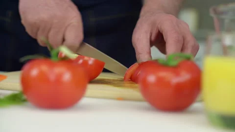 Elderly man cuts tomato into cubes on wooden cutting board Video stock 239085948