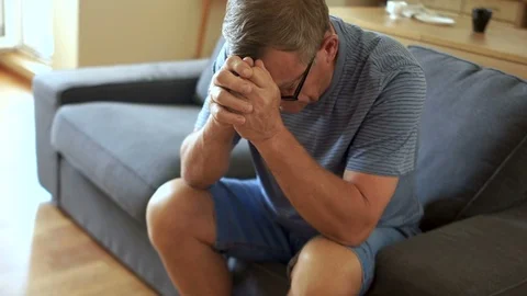 An elderly man in depression is sitting on the couch. He lowered his head, the Stock Footage 93997591