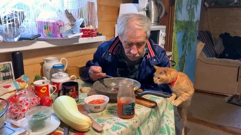 An elderly man dines in the kitchen with a red cat Stock-Footage 116648715