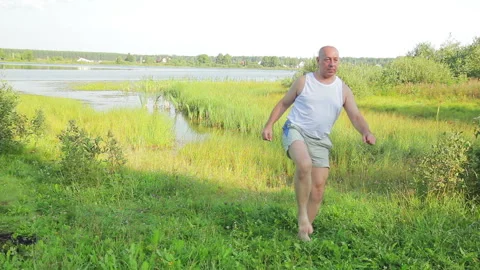 An elderly man does exercises on his feet on the lake in the morning Stock Footage 119278791