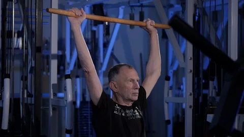 An elderly man does an isometric exercise with a stick, holding it over his head Video stock 115846221