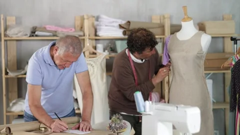 Elderly man drawing pattern on paper male assistant sews on mannequin Stock Footage 329394651